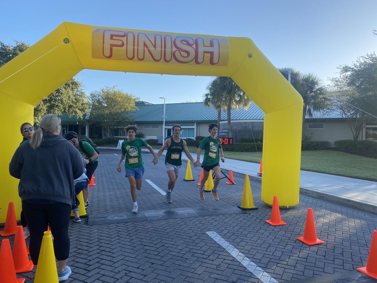 Left to right: sophomore Luca Sandschafer, senior Luke Heckert, and sophomore Asher Walton cross the finish line hand in hand. All of them are members of the Varsity Boys Cross Country team. Sandschafer, Heckert, and Walton exemplify the spirit of togetherness and connectivity that the Shore to Shorecrest 5k aimed to promote.