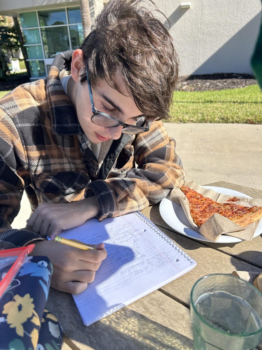 Junior Logan Phares-Robinson eating pizza and working on homework during lunch.