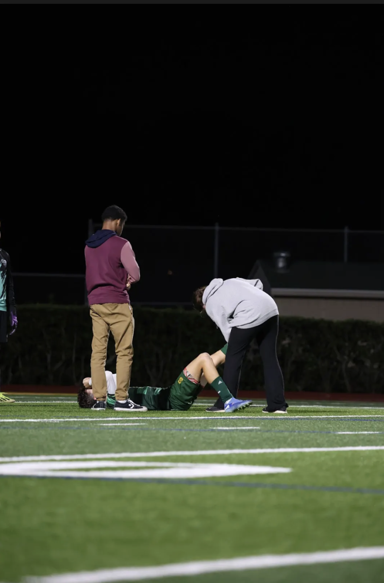 Athletic trainer Sydney Vyer stretches a varsity boys soccer player after getting injured during a match. New this year, students have the opportunity to shadow Vyer during home sports games.
